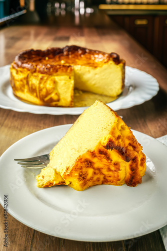 Famous San Sebastian cheesecake displayed on a Basque bar counter. Whole cake with a caramelized top and visible creamy interior, showcasing its iconic texture, with a portion served on a white plate.