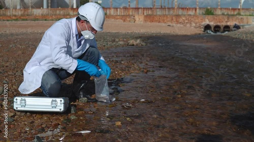 man in a protective suit takes a sample of water from the river after the release of chemical waste