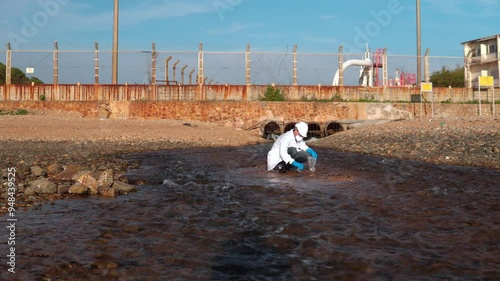 man in a protective suit takes a sample of water from the river after the release of chemical waste