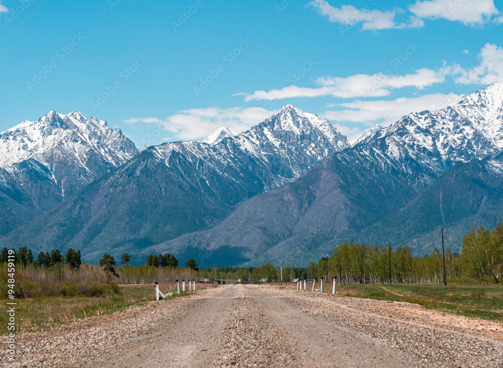 Naklejka premium A winding gravel road leading toward snow-capped mountains