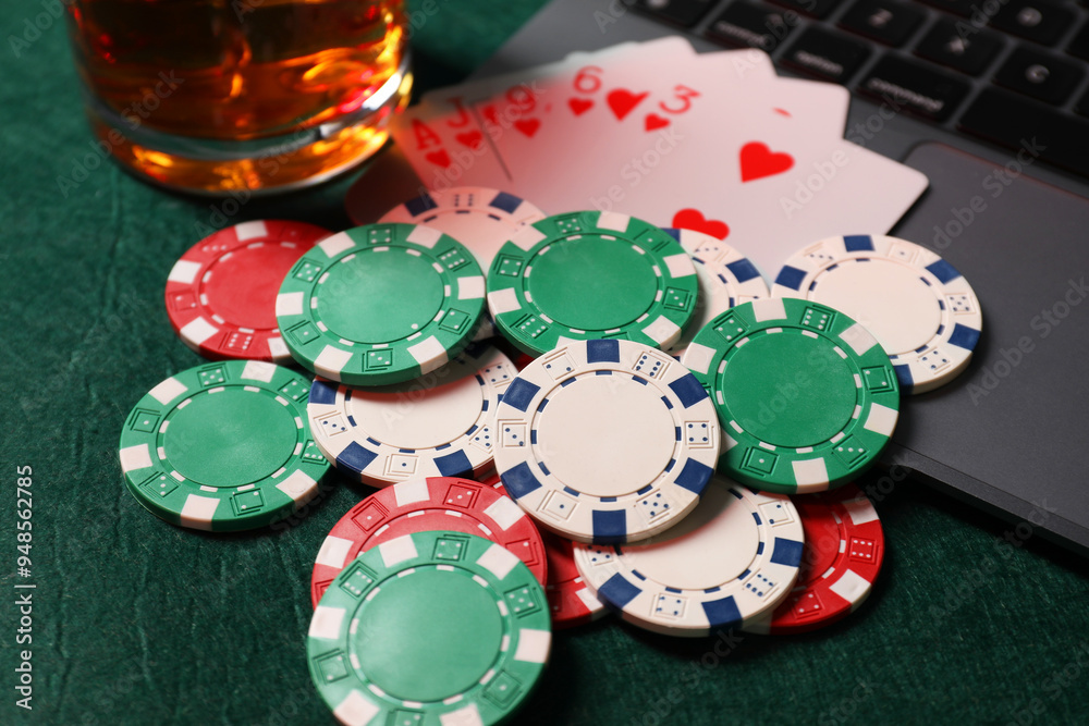 Poker chips, laptop, playing cards and glass of alcohol drink on green table, closeup. Online game Poker chips, laptop, playing cards and glass of alcohol drink on green table, closeup. Online game