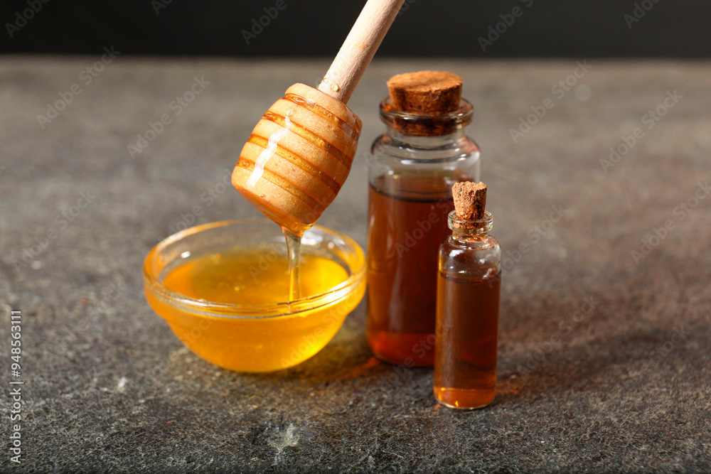 Pouring honey from dipper into bowl and bottles of tincture on grey textured table, closeup. Alternative medicine Pouring honey from dipper into bowl and bottles of tincture on grey textured table, closeup. Alternative medicine