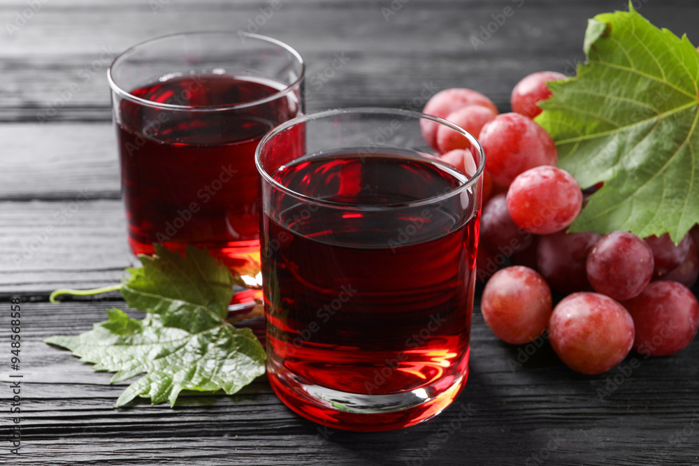 Tasty grape juice in glasses, leaves and berries on black wooden table, closeup Tasty grape juice in glasses, leaves and berries on black wooden table, closeup