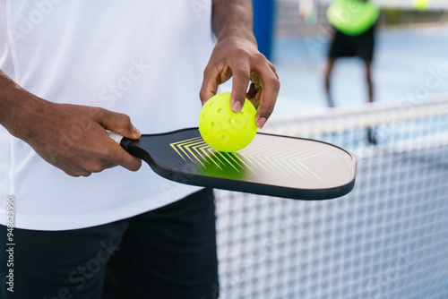 Close-up of pickleball paddle and ball in African American player's hand, outdoor game