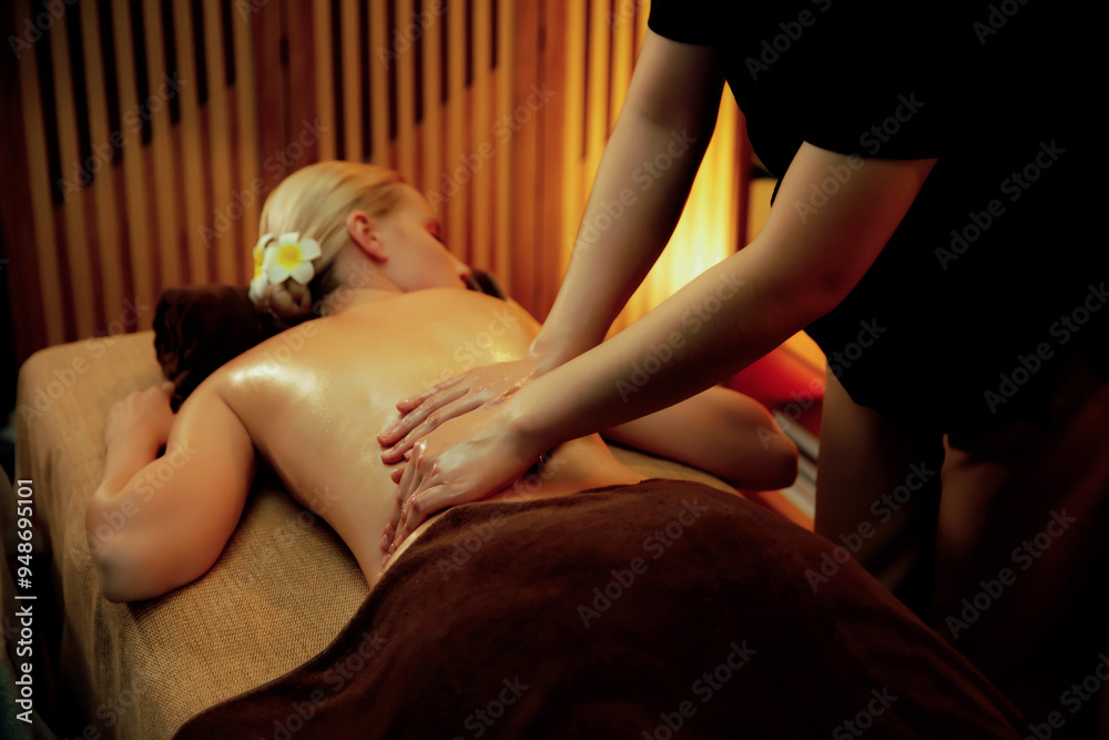 Fototapeta premium Caucasian woman customer enjoying relaxing anti-stress spa massage and pampering with beauty skin recreation leisure in warm candle lighting ambient salon spa at luxury resort or hotel. Quiescent
