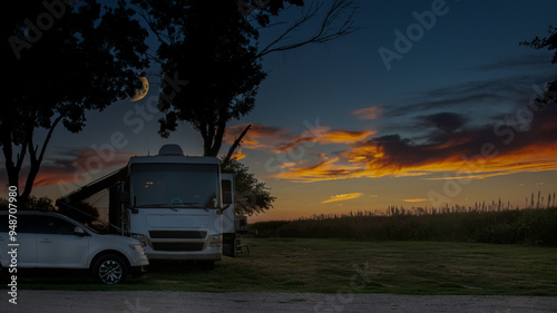 Rv motorhome parked at campsite under a rising moon and sunset sky 