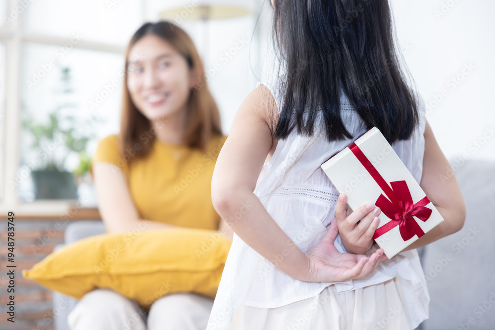 Fototapeta premium Little Girl Hiding Gift Box at Her Back Trying to Surprise Her Mother