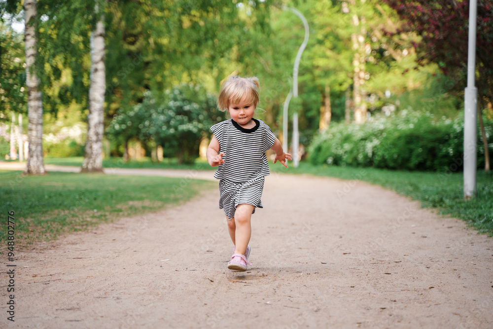 Cute Caucasian toddler child 2-years-old girl walks in a green park at sunset in summer. The concept of a joyful childhood and active pastime. Cute Caucasian toddler child 2-years-old girl walks in a green park at sunset in summer. The concept of a joyful childhood and active pastime.