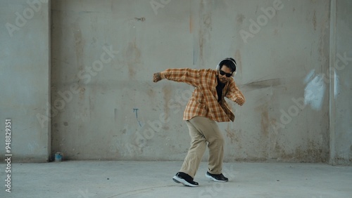 Attractive hispanic dancer in casual look practice street dance while listen music from headphone at cement background. Motion shot of break dancing performance. Outdoor sport 2024. Hiphop.