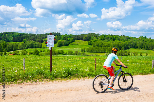 Obraz na płótnie Woman cyclist riding bicycle on gravel rural road among green meadows, Suwalski Landscape Park, Podlasie, Poland w salonie