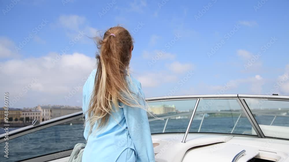 Portrait of beautiful happy blond long haired caucasian woman in blue shorts suit on white deck of speedboat sailing on wide river in city. Real time handheld video. Leisure activity theme. Portrait of beautiful happy blond long haired caucasian woman in blue shorts suit on white deck of speedboat sailing on wide river in city. Real time handheld video. Leisure activity theme.