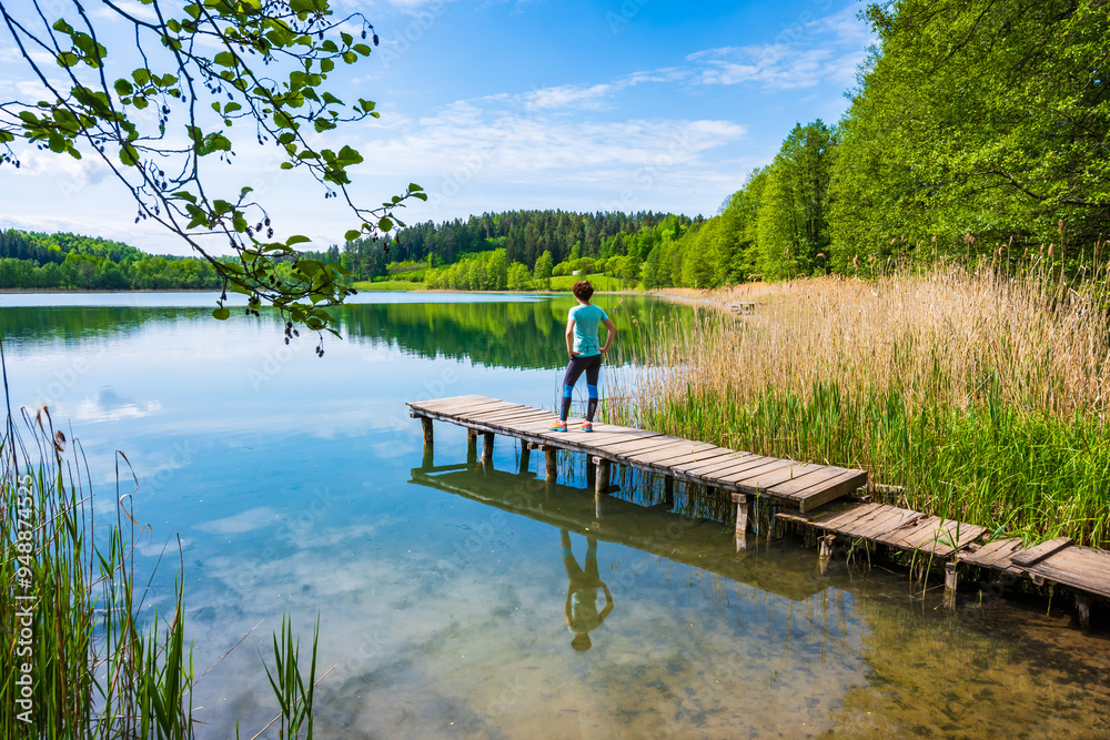 Fototapeta premium Woman tourist standing on wooden pier on shore of Wigry lake, Wigry National Park, Podlasie, Poland