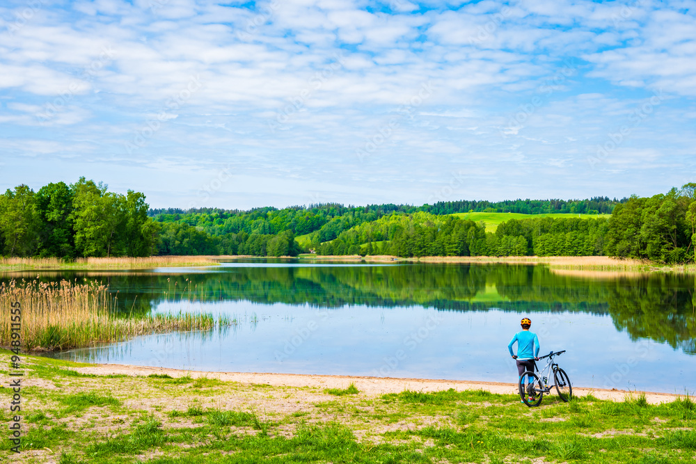 Woman cyclist tourist standing on beach shore of Pobondzie lake, Suwalski Landscape Park, Podlasie, Poland Woman cyclist tourist standing on beach shore of Pobondzie lake, Suwalski Landscape Park, Podlasie, Poland