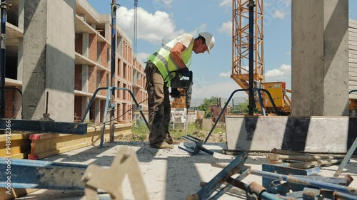 Construction Worker Using Power Tool on Site. A construction worker operates a power tool while working on an outdoor construction site. photo