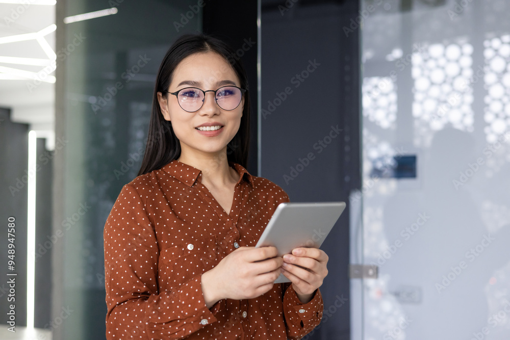Confident Asian worker in modern office environment holding tablet. Dressed in polka dot blouse , she exhibits friendly and professional demeanor, representing diverse workforce in corporate setting Confident Asian worker in modern office environment holding tablet. Dressed in polka dot blouse , she exhibits friendly and professional demeanor, representing diverse workforce in corporate setting