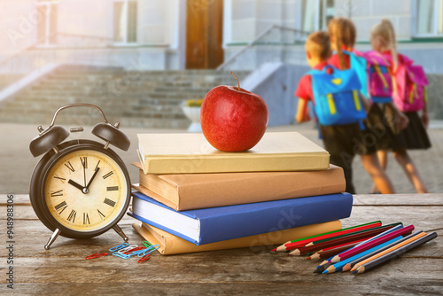 School books with apple, stationery and alarm clock on table against white ba...