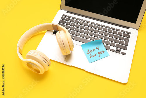 Sticky note with text DON'T FORGET, laptop and headphones on yellow background