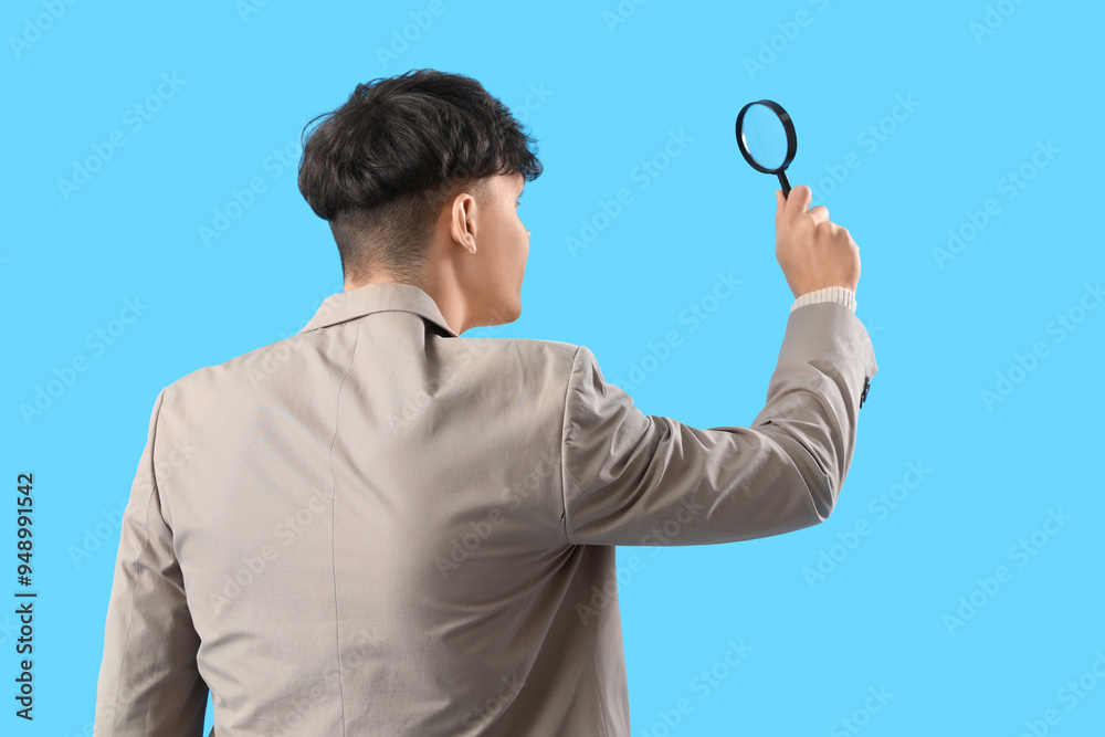 Young man with magnifier on blue background, back view Young man with magnifier on blue background, back view