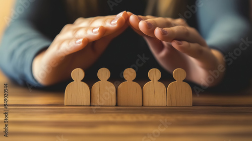 Woman's hands protecting wooden people icons on a table, for a business team or family protection photo