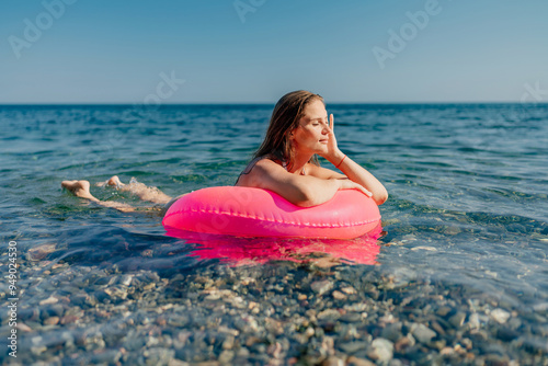 A woman is laying in a pink inflatable tube in the ocean