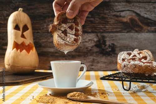 An unrecognisable man picking up a pumpkin-shaped biscuit and dipping it in milk, in the background a Halloween pumpkin. photo