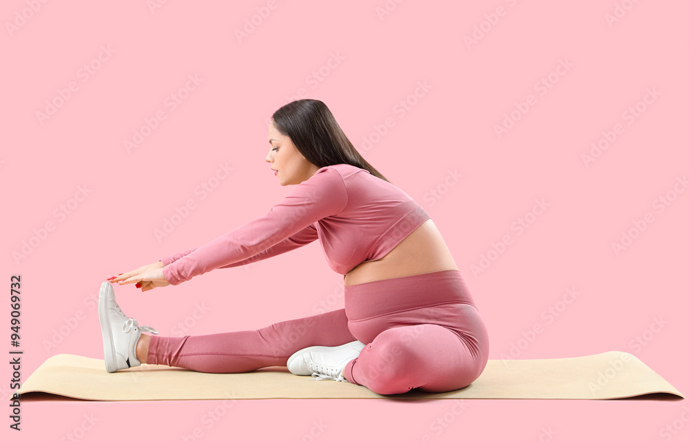 Sporty pregnant woman stretching on mat against pink background Sporty pregnant woman stretching on mat against pink background