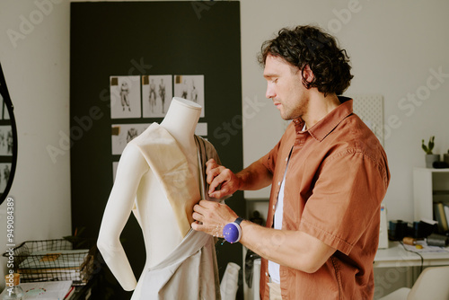 Curly haired tailor doing dart on fabric painstakingly in modern atelier photo