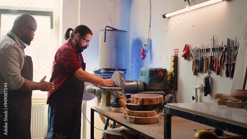 Man teaching african american trainee how to shape wooden bowl on disc sander in assembling shop. Worker learning from woodworking professional how to use grinding machine rotating disc, camera B