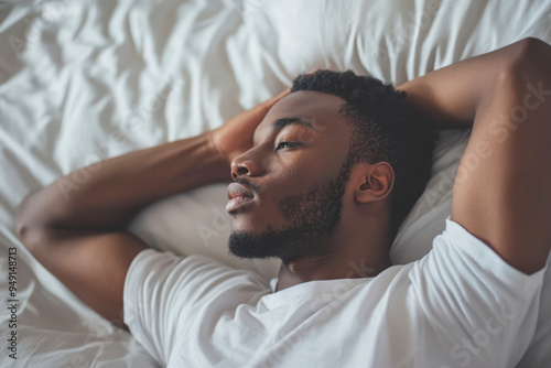 Young african american man in nightwerar hold hand behind neck lying in bed rest relax spend time in bed. photo