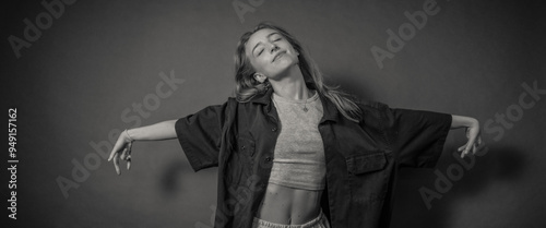 Canvas-taulu A woman is posing gracefully with her arms extended, wearing a loose shirt and crop top, against a minimalistic background, creating a sense of freedom and artistic expression