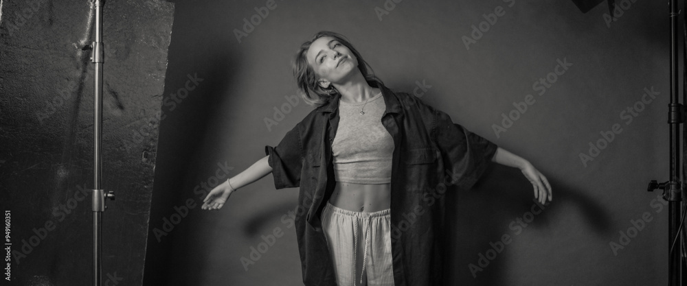 Obraz premium A black and white image of a woman posing with her arms outstretched in a studio, wearing casual clothes, conveying a sense of freedom and expression through body language.