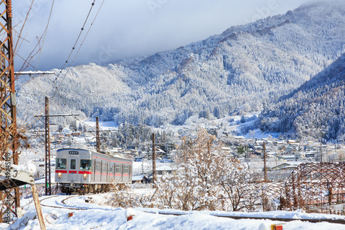 雪が積もった焼額山を背景に長野電鉄が大カーブを進む