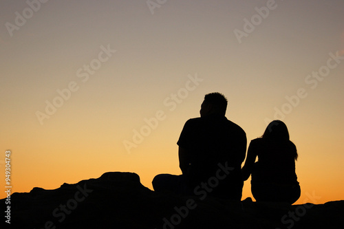 A young couple, rendered in silhouette, watches the sunset while sitting on a rock at the shore in Laguna Beach, California