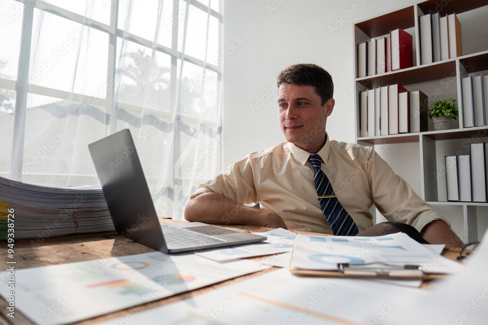Young Businessman Sitting and Working in a Modern Office with Documents and Laptop on Desk Young Businessman Sitting and Working in a Modern Office with Documents and Laptop on Desk