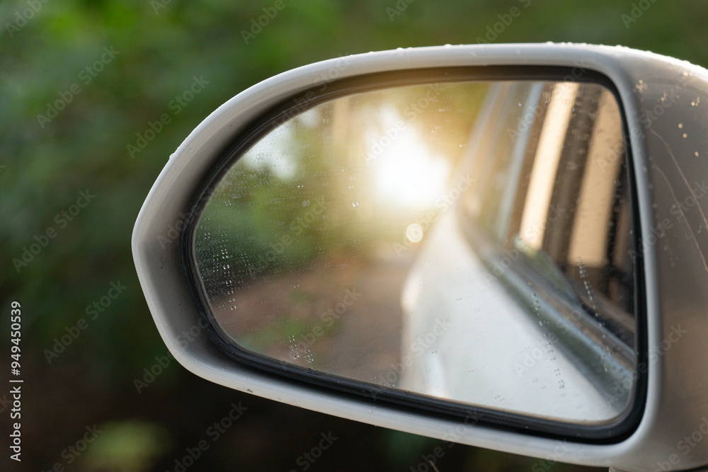 View miror of white car with sunlight. background of green tree.