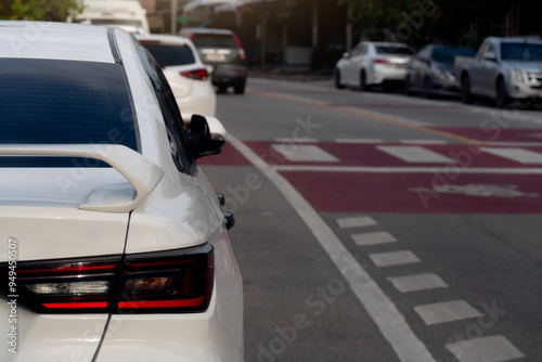 Tail lights of white car parking beside road. Road with traffic lines for safety when crossing roads in the city.