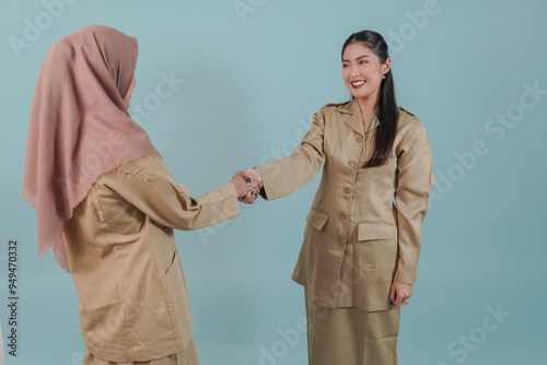 Two smiling Indonesian government worker women wearing khaki uniform doing handshake gesture. photo