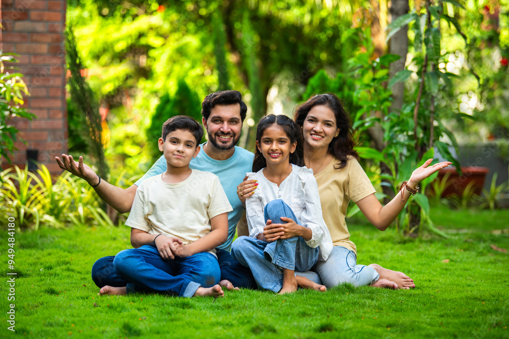 Happy Indian family of four sitting in park, embracing and smiling at camera, enjoying quality time Happy Indian family of four sitting in park, embracing and smiling at camera, enjoying quality time
