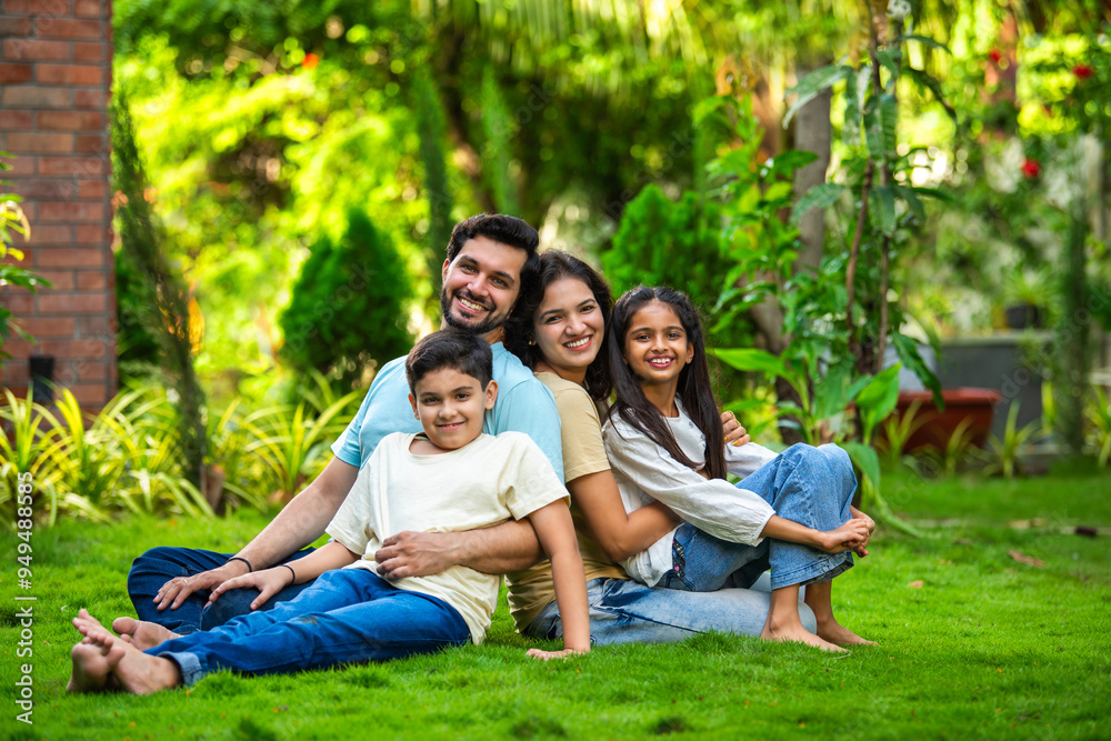 Happy Indian family of four sitting in park, embracing and smiling at camera, enjoying quality time