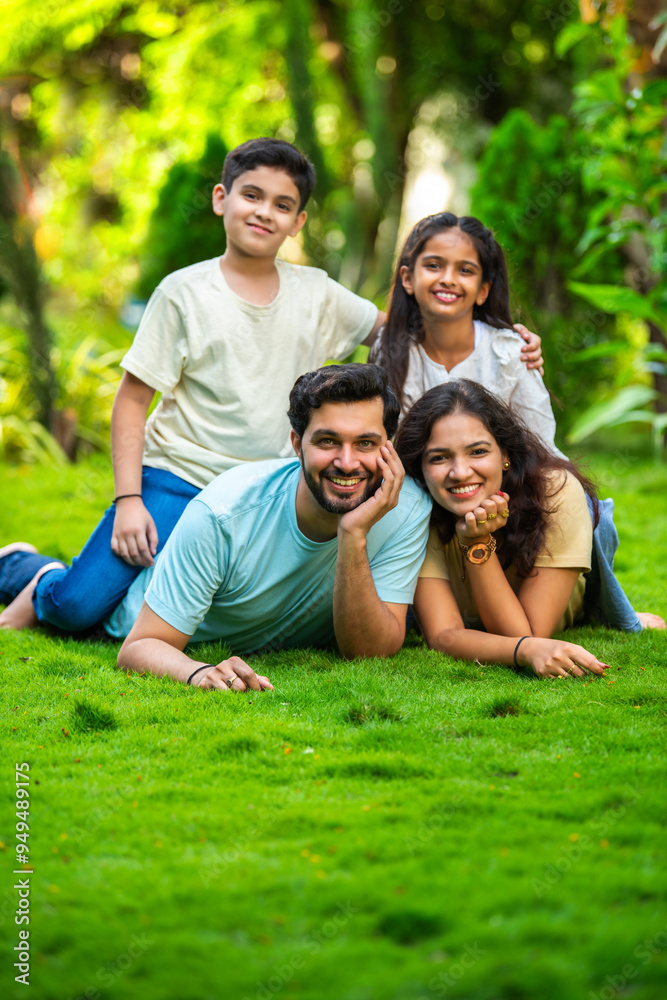 Happy Indian family of four sitting in park, embracing and smiling at camera, enjoying quality time Happy Indian family of four sitting in park, embracing and smiling at camera, enjoying quality time