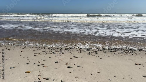 Pebble beach with red tide waves and ships out at sea on the blue horizon photo