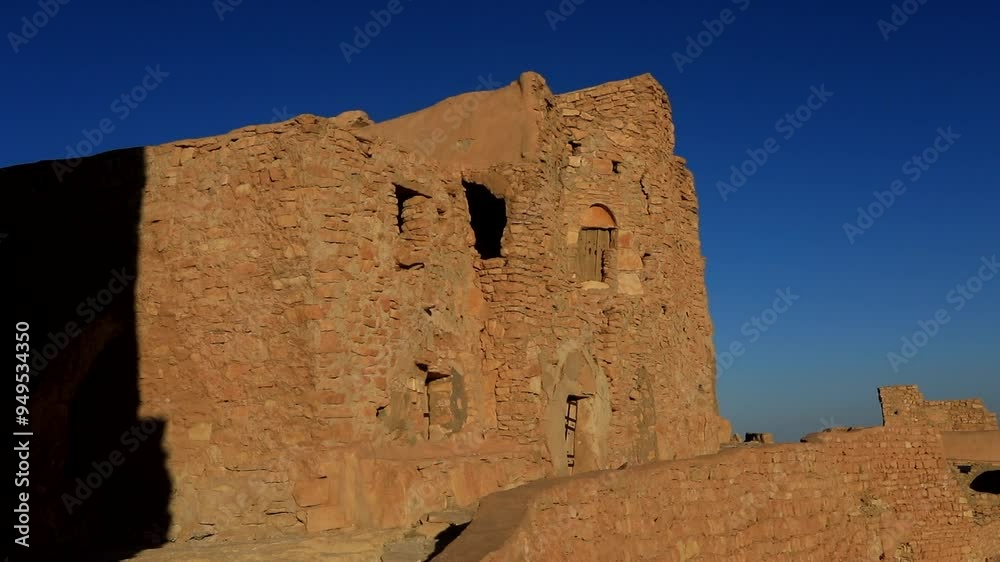 An ancient stone building in Tunisia under a clear blue sky with deep shadows at sunset An ancient stone building in Tunisia under a clear blue sky with deep shadows at sunset