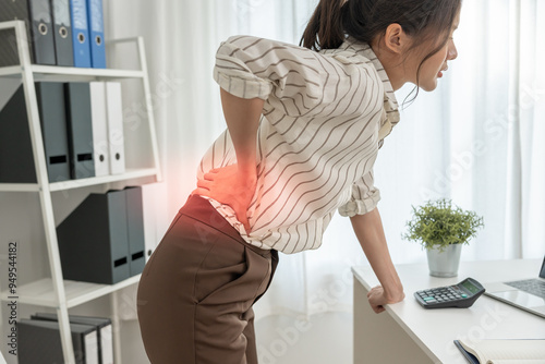 Asia beautiful woman holding her lower back while and suffer from unbearable pain health and problems, chronic back pain, backache in office syndrome, scoliosis, herniated disc, muscle inflammation photo