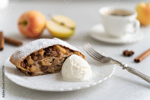 Freshly baked powdered apple strudel with raisins and ice cream on white plate with red apples and cinnamon on white background. homemade Apfelstrudel, austrian germany cuisine. Menu, recipe, close up