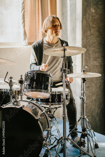 Drummer playing drum set in recording studio. Focused musician performing on drums, surrounded by professional equipment, vertical image photo