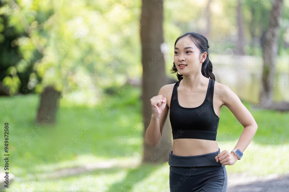 Energetic Asian woman jogging through green park trail Energetic Asian woman jogging through green park trail