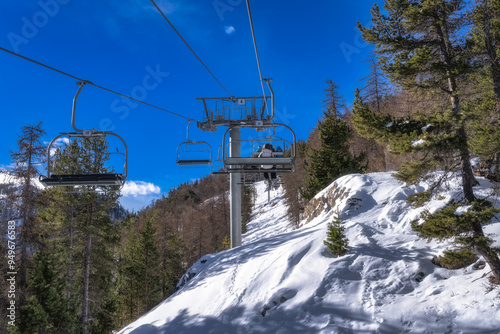 People riding up on a ski lift to hit early slopes covered in fresh snow, Montgenevre ski village on border of France and Italy. Winter sport in Alps