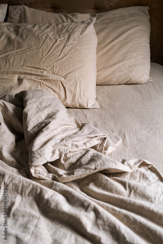 Empty bed covered wrinkled bedding and pillows in cozy bedroom at nighttime.