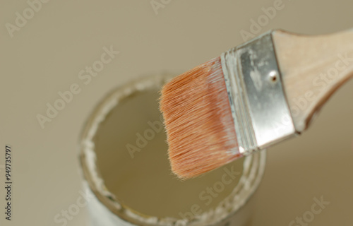 Close-up of a paintbrush above a white paint can, focusing on the bristles and handle. The image captures a painterly moment, showcasing the tool's texture and details