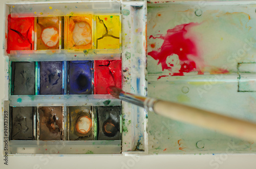A brush blending color in a watercolor paint box, showing vibrant hues and a creative process in progress